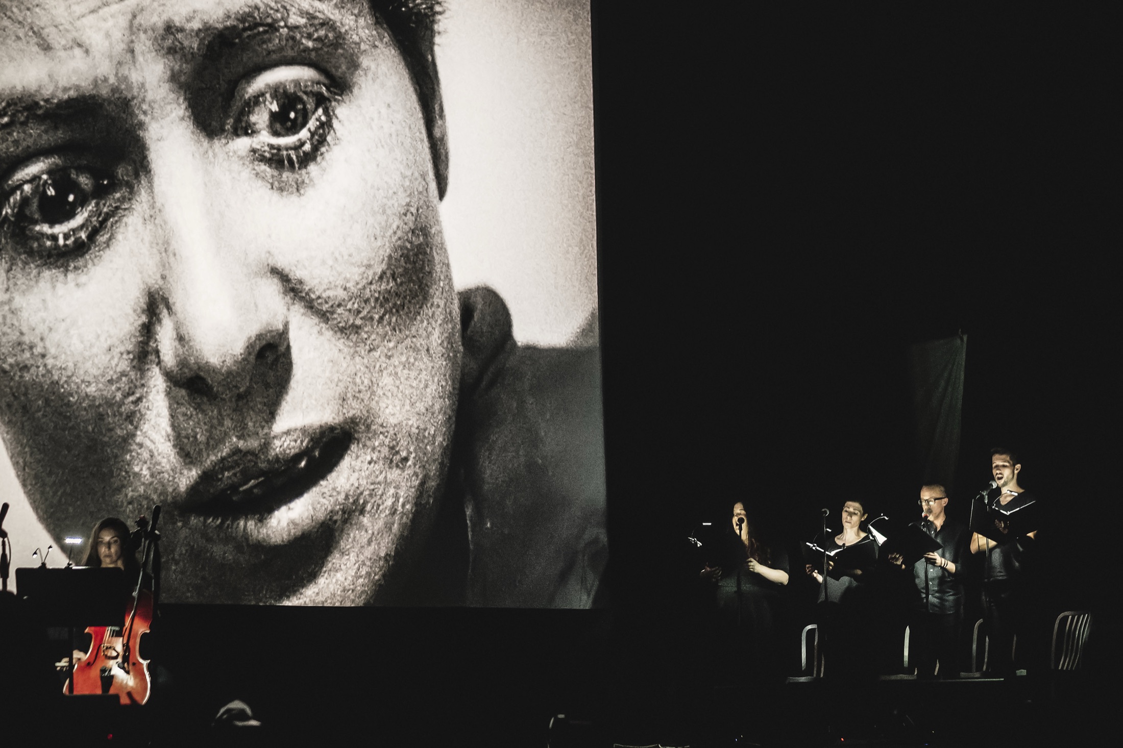 Verdigris singers beside a large archival face projection