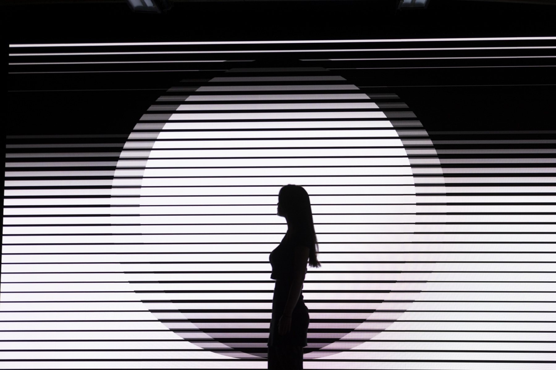 Visitor silhouetted in front of a circular NONOTAK light installation