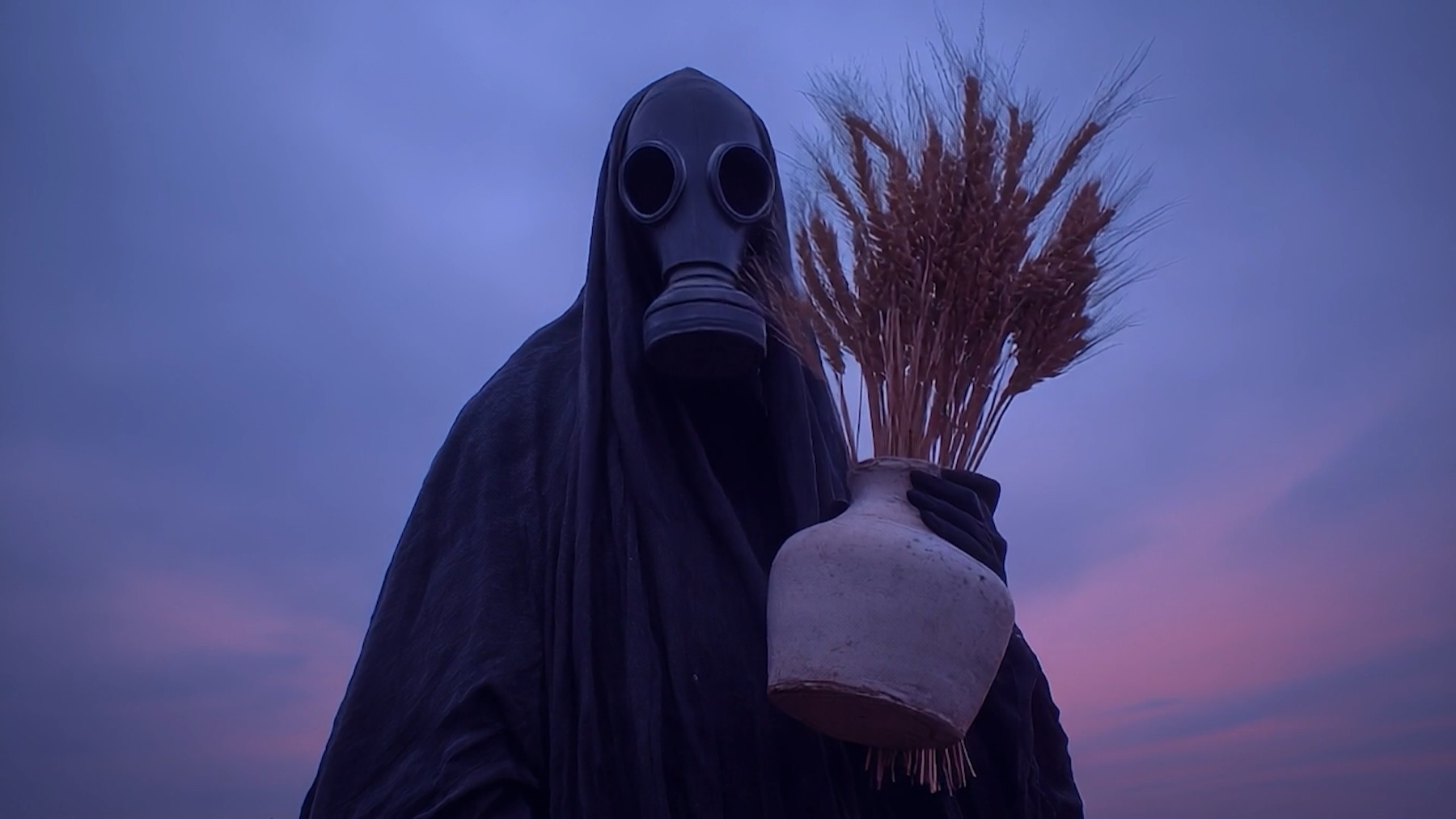 Still from Gurbet showing a masked figure holding a vessel at dusk